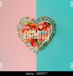 Creative heart made of gummy candies and sprinkles on pastel pink and ...
