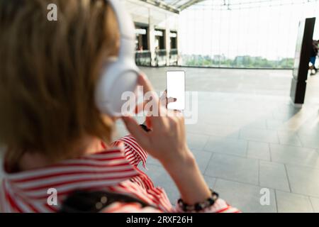 Woman listening to music on headphones and holding a mobile phone in a shopping mall. Stock Photo