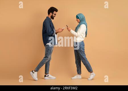 Muslim Dating Apps. Young Islamic Couple With Smartphones Walking Toward Each Other Stock Photo