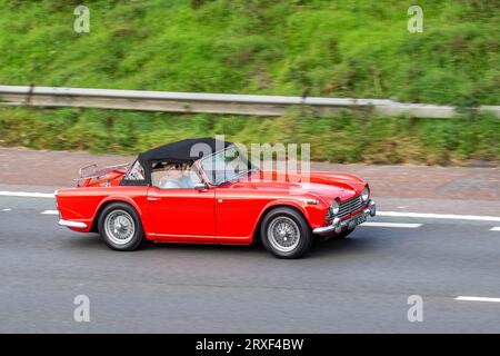 1965 60s sixties Red Triumph Tr4a Red Petrol 2138 cc, four-speed manual, four-cylinder petrol engine sports car; travelling at speed on the M6 motorway in Greater Manchester, UK Stock Photo