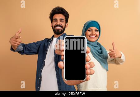 Nice Offer. Smiling Muslim Couple Showing Big Blank Smartphone In Their Hands Stock Photo