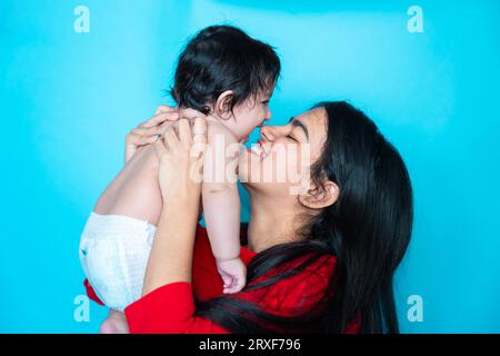 Indian teenager girl playing six months cute little baby in diaper isolated over blue background. Asian infant child and sister, Happy family. Stock Photo