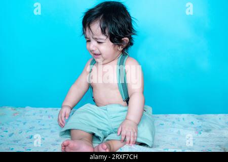 Smiling six months old cute indian baby boy sitting isolated over blue studio background, Happy child with black hair. Stock Photo