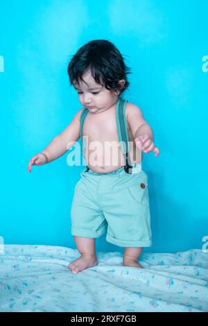 Smiling six months old cute indian baby boy trying isolated over blue studio background, Happy child with black hair. Stock Photo