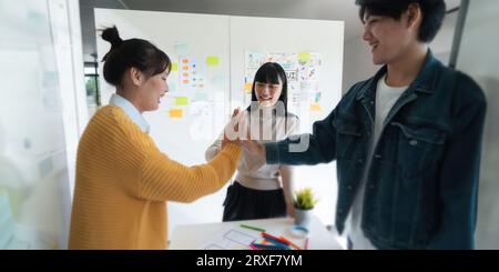 Asia team creative in smart casual wear discussing phone application design celebrate giving five after dealing feeling happy in office. coworker Stock Photo