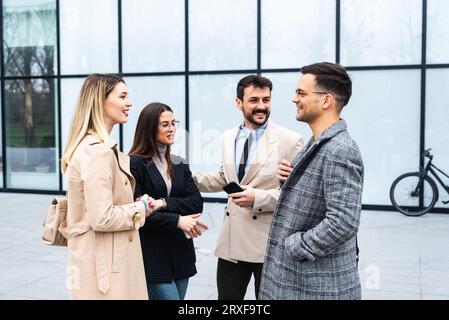 Group of business people walking outside in front of office building. Colleagues discussing on the way to the work. Young employees talking about staf Stock Photo
