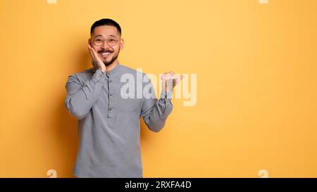 Amazed Young Asian Man Touching Head And Pointing Aside At Copy Space Stock Photo