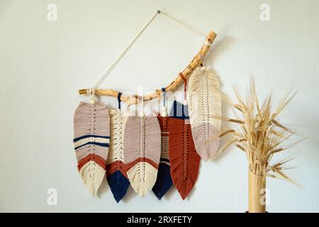 Wall panel in Boho style made of cotton beige, blue and red cords using macrame technique. Modern home decor trend, cozy atmosphere, boho style. Stock Photo