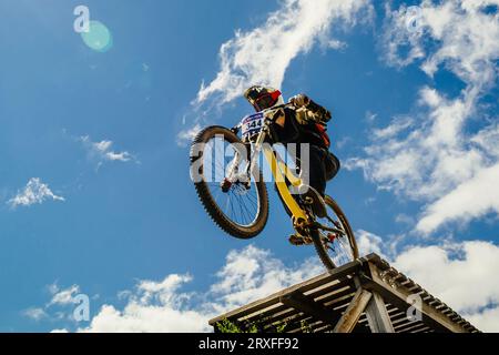 athlete mountainbiker edge of drop downhill in background of blue sky Stock Photo