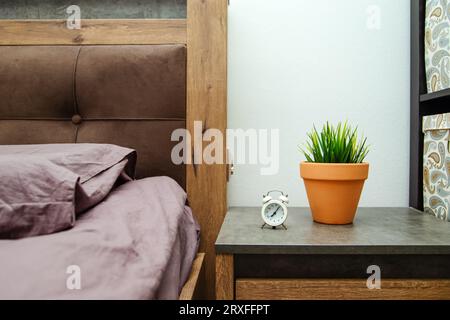 Alarm clock on the bedside table by the bed. Modern bedroom interior, details. Stock Photo