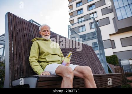 Elderly man sitting on bench, resting after his morning run. Stock Photo