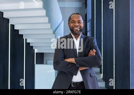Portrait of mature and successful businessman inside office, boss smiling and looking at camera with crossed arms, african american man in business suit happy with successful achievement results. Stock Photo