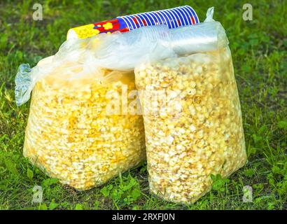 Popcorn in transparent big packages on a grass. It is a lot of snacks and popcorn Stock Photo