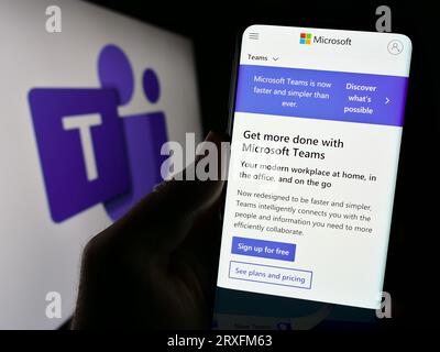 Person holding smartphone with webpage of business communication platform Microsoft Teams on screen with logo. Focus on center of phone display. Stock Photo