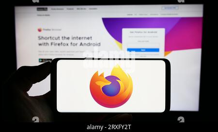 Person holding mobile phone with logo of open-source web browser Mozilla Firefox on screen in front of web page. Focus on phone display. Stock Photo