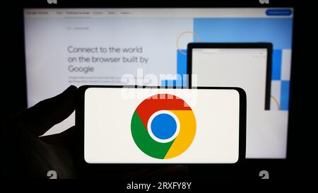 Person holding smartphone with logo of web browser Google Chrome on screen in front of website. Focus on phone display. Stock Photo