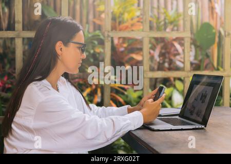 Freelancer woman using smartphone and laptop computer in summer cafe Stock Photo