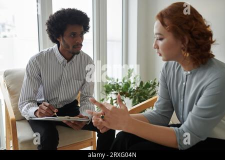 Psychologist taking notes in document when listening to client describing her problem Stock Photo