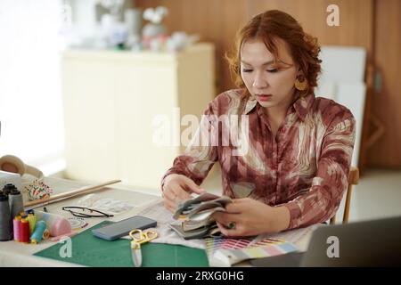 Pensive young woman looking over fabric samples when working on new project Stock Photo