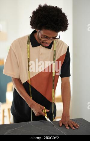 Smiling tailor cutting piece of fabric when working on dress Stock Photo