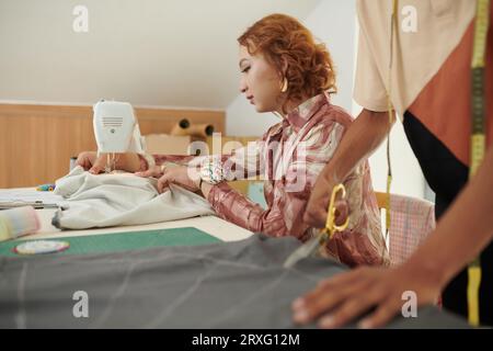 Creative young woman using sewing machine when making gown for client Stock Photo