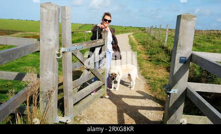 Female dog walker opening gate to allow others to pass through, Cornwall, UK - John Gollop Stock Photo