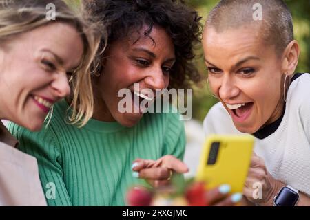 Photo of three multiethnic mature women looking at one mobile together surprised. Stock Photo
