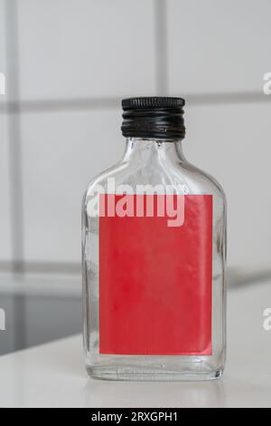 Flat empty glass bottle with empty red label on a kitchen counter , white background Stock Photo