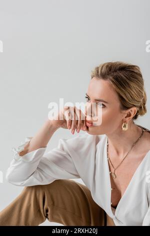 close up beautiful woman in formal pastel clothing sitting on floor touching her face, fashion Stock Photo