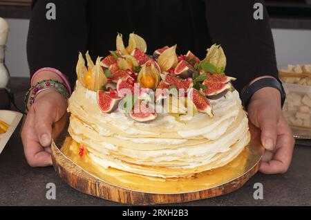 Midsection body of vendor showing crepe cake beautifully decorated with fresh figs, Peruvian cherries and pomegranate seeds. Stock Photo