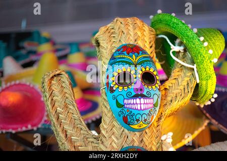 Straw cactus with Mexican blue skull mask and background of colored hats Stock Photo