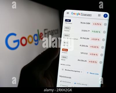 Person holding smartphone with webpage (German) of financial information platform Google Finance on screen. Focus on center of phone display. Stock Photo