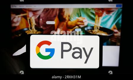 Person holding smartphone with logo of mobile payment service Google Pay on screen in front of website. Focus on phone display. Stock Photo
