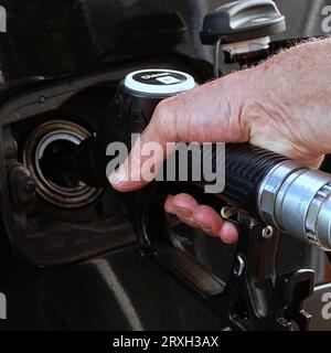 Refueling the car, a man's hand refills diesel fuel at the gas station and the gasoline pump fills the fuel nozzle in the car tank. Stock Photo