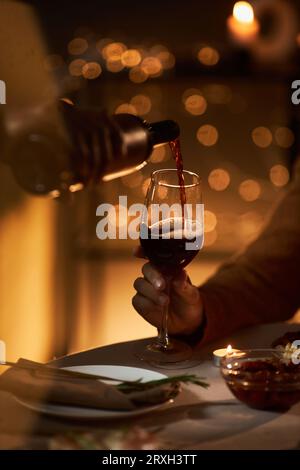 Close up of couple pouring red wine into glass during romantic dinner in dark Stock Photo