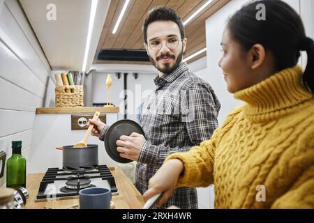 Side view portrait of young couple cooking together in trailer van while travelling together Stock Photo
