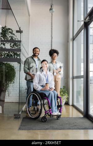 group shot of diverse and inclusive business people looking at camera, wheelchair user in office Stock Photo