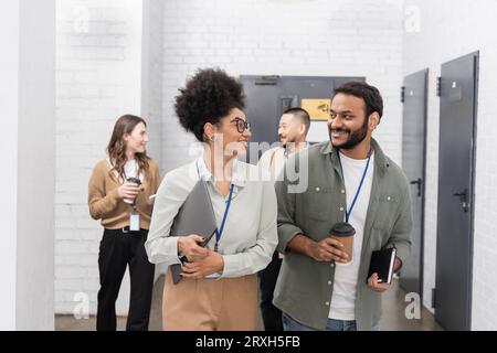 happy african american woman and indian man chatting during coffee break near diverse colleagues Stock Photo