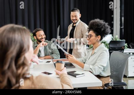 happy african american team leader holding documents and discussing project with colleagues Stock Photo