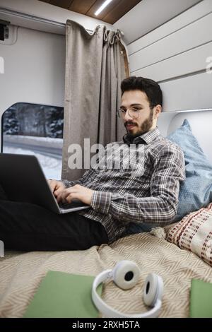 Vertical portrait of bearded man working in trailer van using laptop on bed Stock Photo