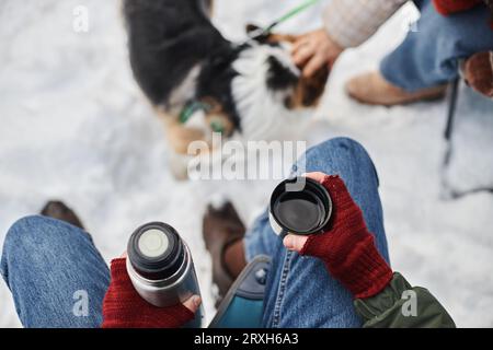 Top view closeup of young man holding thermos with hot drink while travelling outdoors in winter, copy space Stock Photo