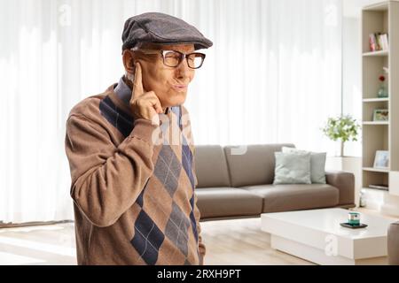Elderly man protecting his ear from an unpleasent sound at home in a living room Stock Photo