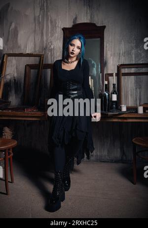 Indoors portrait of beautiful goth girl in black dress. Blue