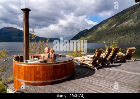 Couple sharing a tender moment while sitting in a wood fired hot tub on the shore of a Yukon Lake; Yukon, Canada Stock Photo