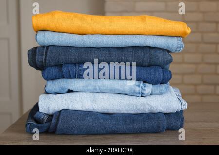A neatly folded stack of clothes after washing - jeans in different shades of blue and a bright yellow sweater on top. Stock Photo
