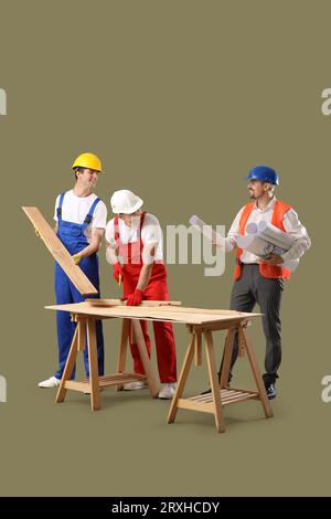 Team of male builders with wooden planks and house plans on green background Stock Photo