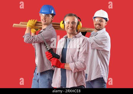 Team of male builders with wooden planks on red background Stock Photo