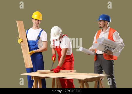Team of male builders with wooden planks and house plans on green background Stock Photo