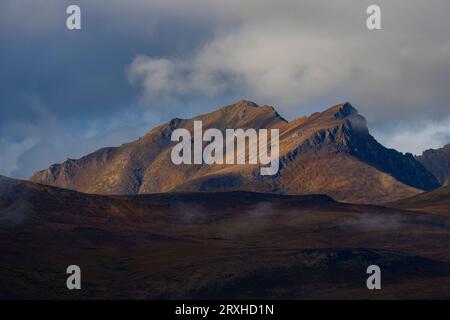 Autumn creeps in slowly after a warm Yukon summer. The mountains are lit up with storm light creating dynamic scenery; Yukon, Canada Stock Photo