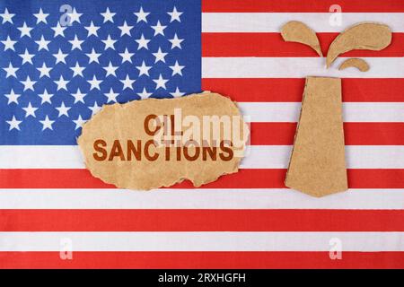 On the US flag there is an oil rig cut out of cardboard and a sign with the inscription - Oil sanctions. Stock Photo